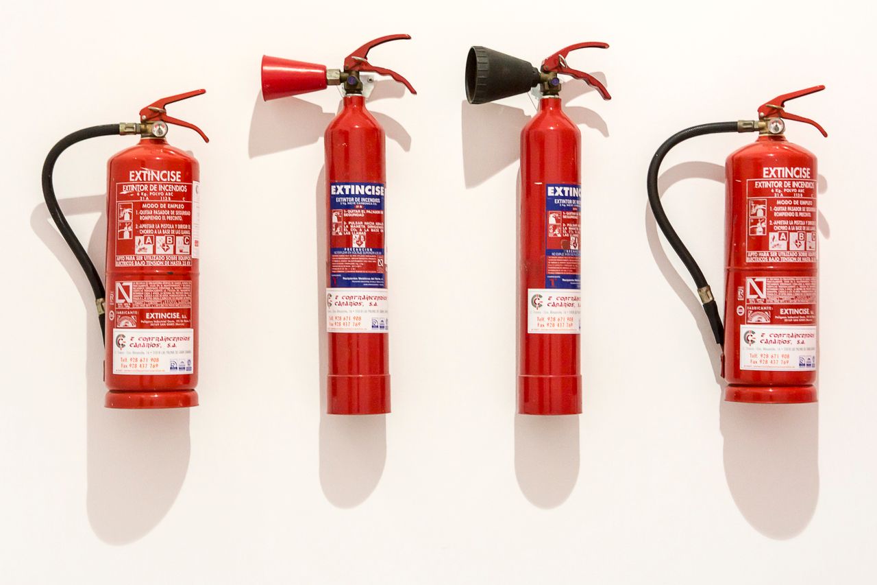 Four red fire extinguishers hanging on a clean white wall in an orderly fashion.